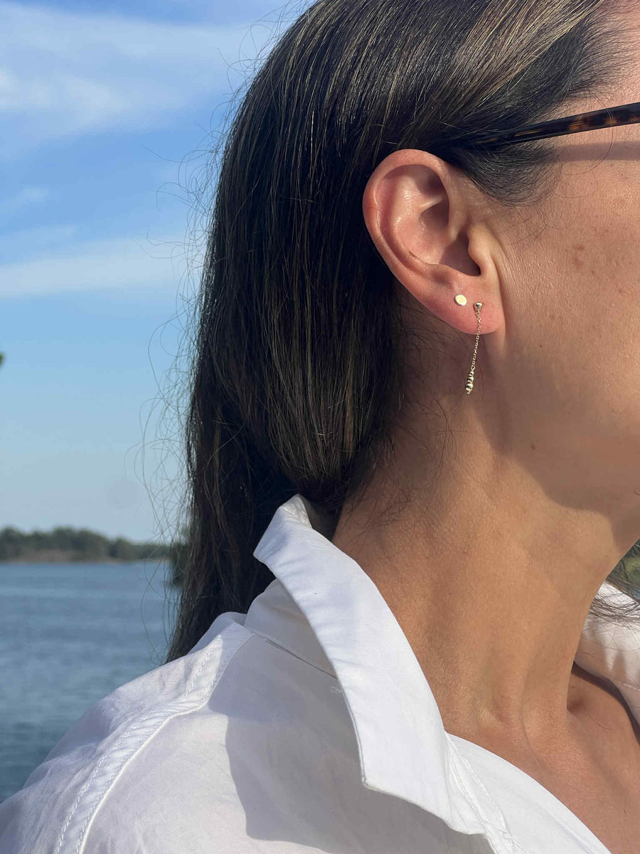 Lätta Viskningar – Aura droppörhängen och Gyllene Cirkel – sfäriska stiftörhängen i 14K massivt guld från Nock Studios, fotograferade vid havet. En lätt kombination med tyngd, en viskning och en punkt.