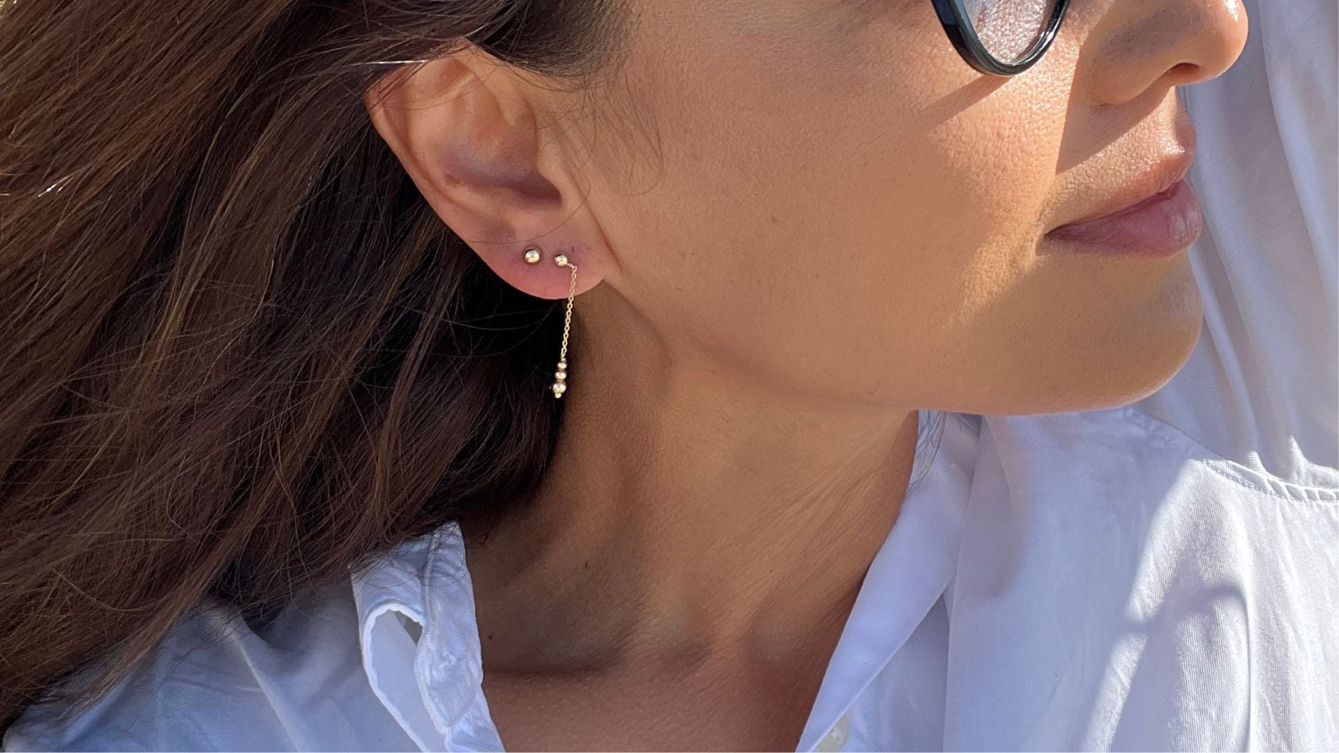 Närbild på kvinna som bär Nock Studios Aura droppörhängen och Nock Sfär studs 3mm i 14K massivt guld – en del av den tidlösa smyckesgarderoben
