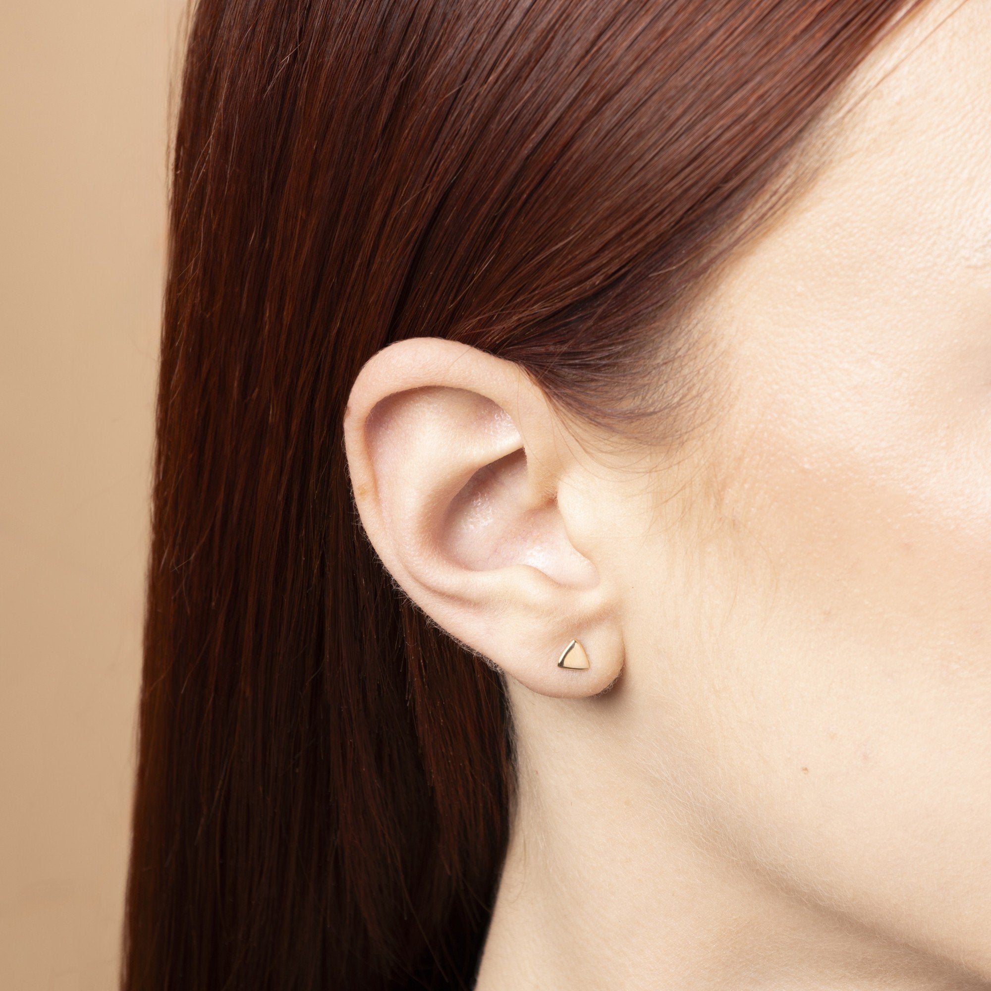 Triangelformade stiftörhängen i 14K guld på kvinna – minimalistiska örhängen från Nock Studios för modern stil och vardagsbruk.

