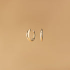 Arcus Hoops Örhängen i 14K guld – designade som mjuka bågar fotograferade mot beige bakgrund