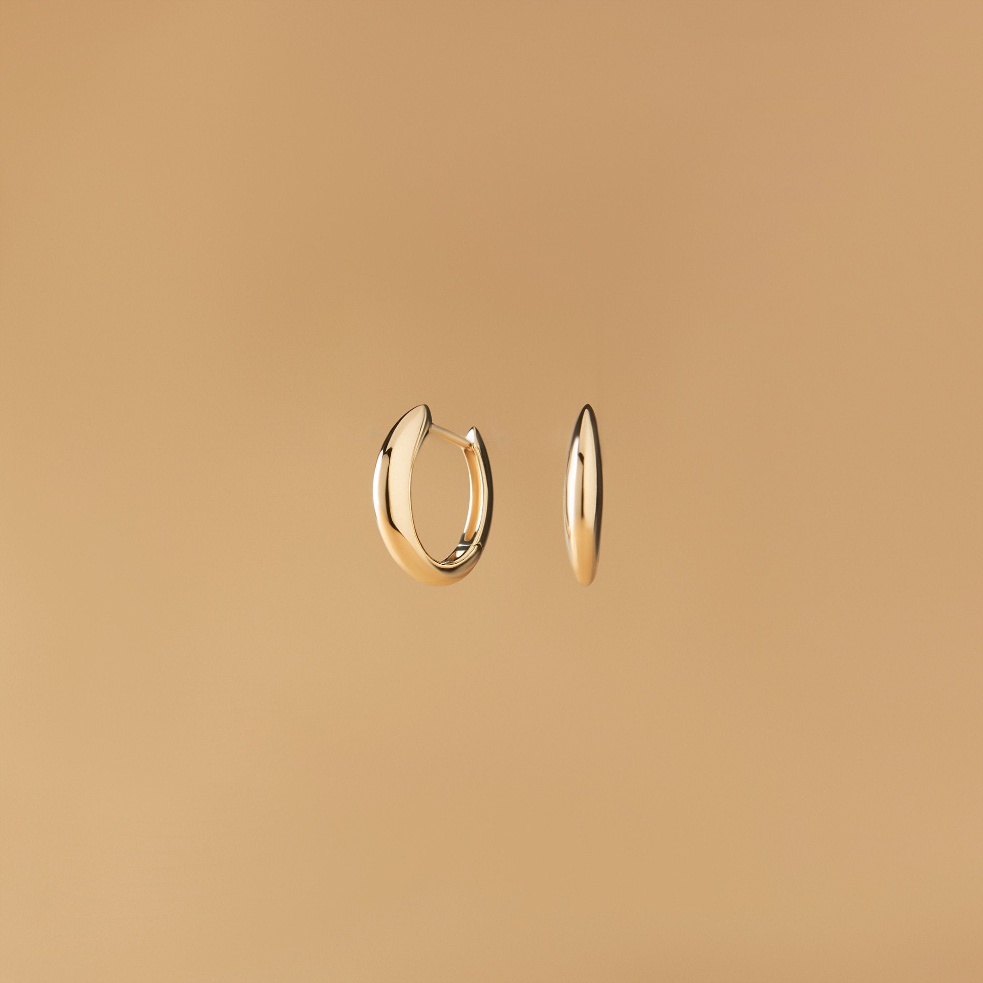 Arcus Hoops Örhängen i 14K guld – designade som mjuka bågar fotograferade mot beige bakgrund