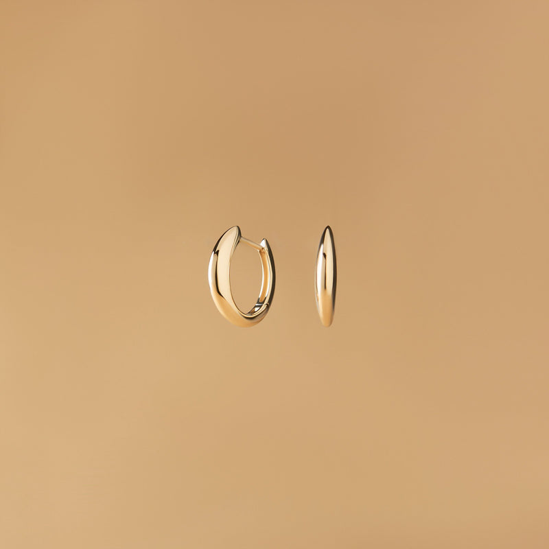 Arcus Hoops Örhängen i 14K guld – designade som mjuka bågar fotograferade mot beige bakgrund