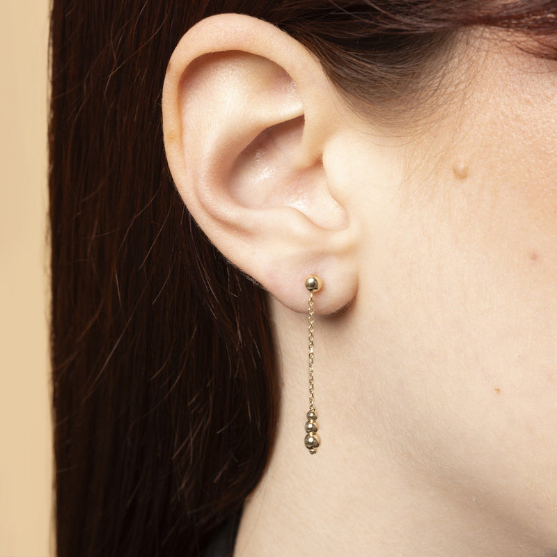 Aura droppörhängen i 14K guld bärs på modell – minimalistisk och sensuell design med tre gyllene sfärer. Nock Studios.