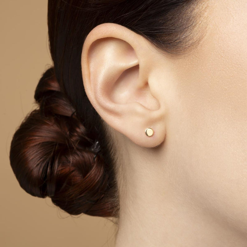Modell bär Gyllene Cirkel – cirkelformade stiftörhängen i 14K guld med polerad yta. Minimalistiska örhängen från Nock Studios.s.