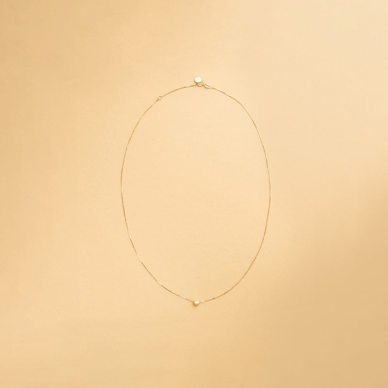 Innersta – hjärthalsband i 14K guld från Nock Studios, fotograferat på ljus bakgrund för att framhäva smyckets minimalistiska design och glans.