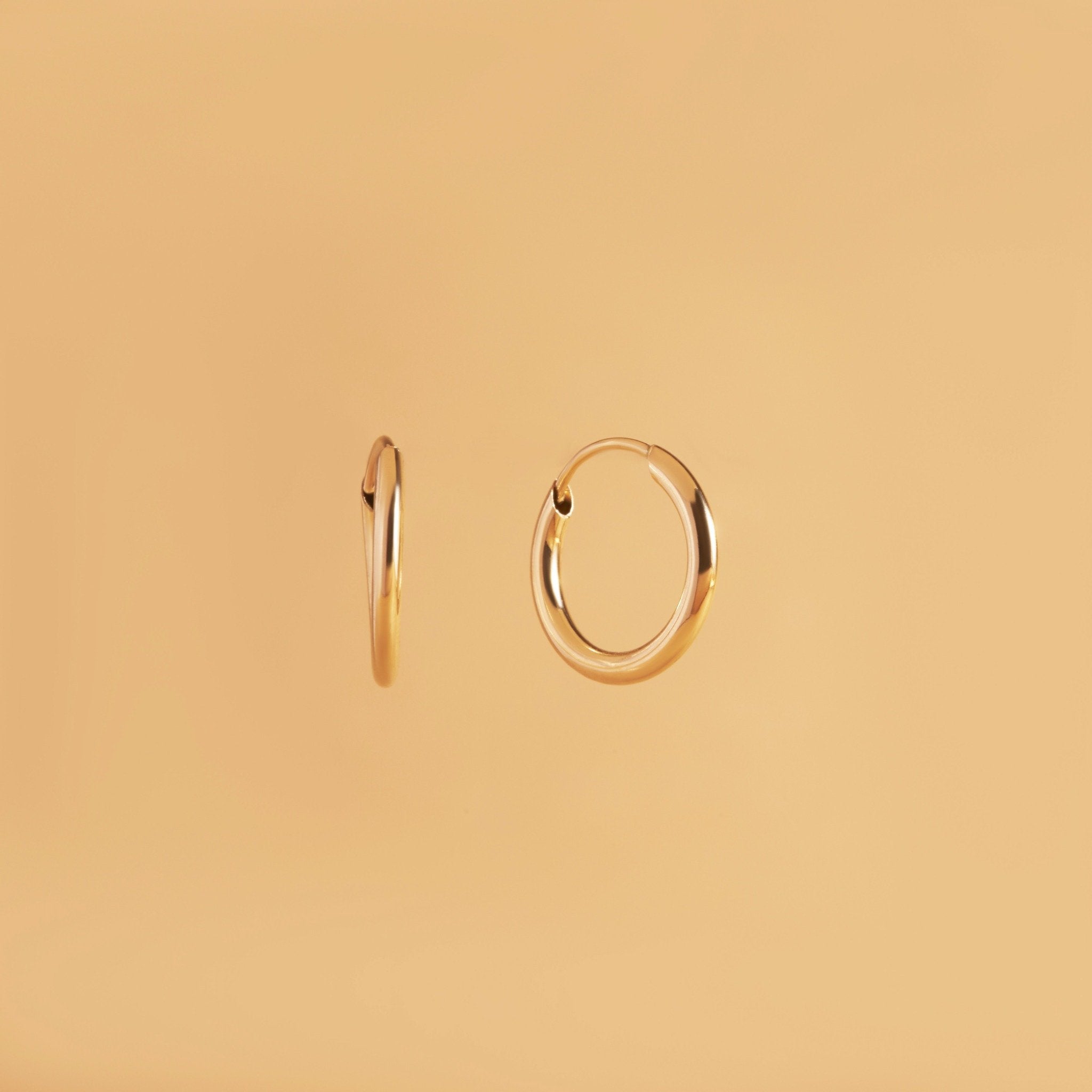 12 mm guldörhängen i 14K – Nock Hoops från Nock Studios. Minimalistisk design med flexrörsteknik för lätt, daglig bärkomfort.