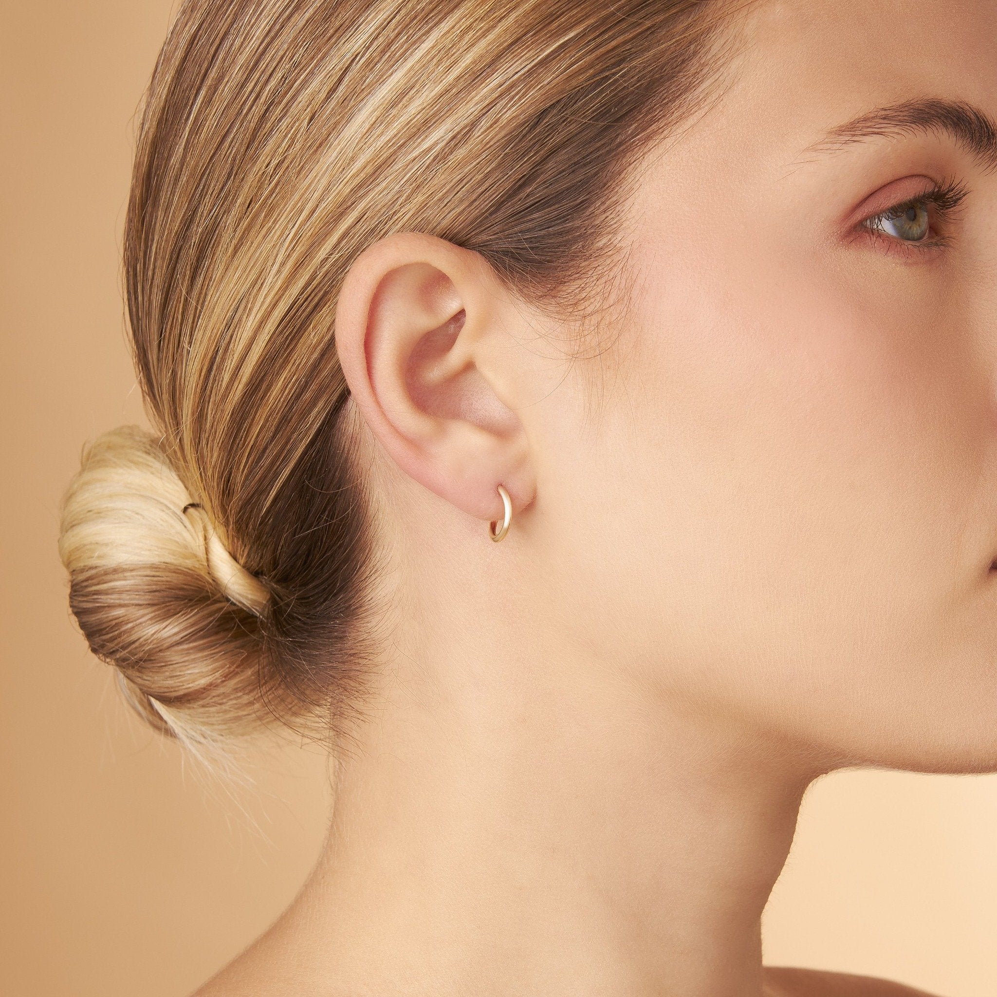 Modell bär Nock Hoops – 12 mm örhängen i 14K guld. Lätt, stilren och diskret design med gyllene närvaro från Nock Studios.