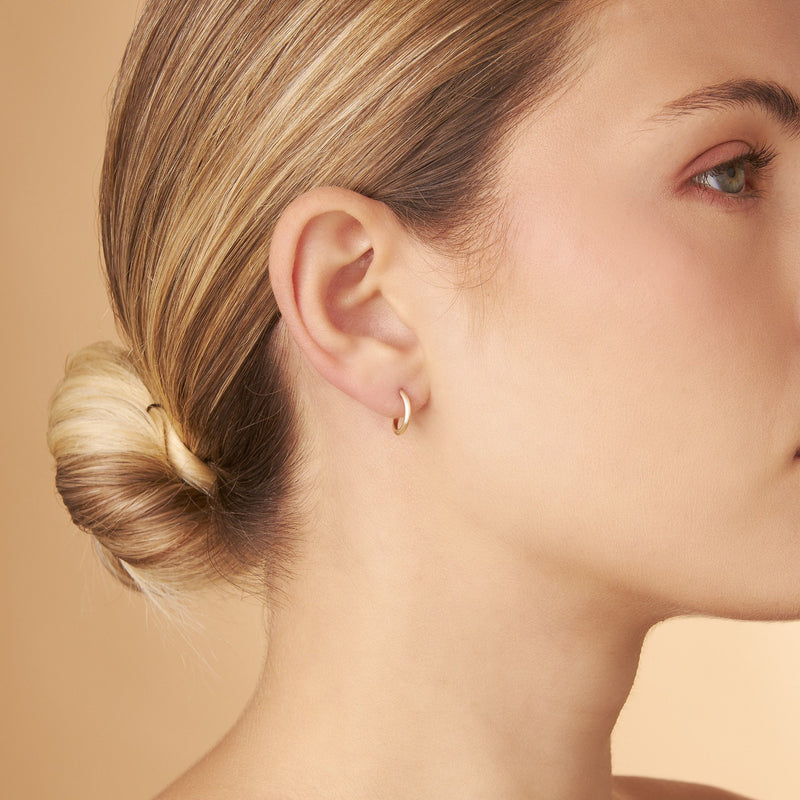 Modell bär Nock Hoops – 12 mm örhängen i 14K guld. Lätt, stilren och diskret design med gyllene närvaro från Nock Studios.