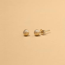 Närbild på sfäriska stiftörhängen i 14K massivt guld – en modern tolkning av klassisk minimalism. Perfekt balans mellan enkelhet och sofistikation.