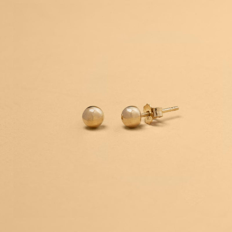 Närbild på sfäriska stiftörhängen i 14K massivt guld – en modern tolkning av klassisk minimalism. Perfekt balans mellan enkelhet och sofistikation.