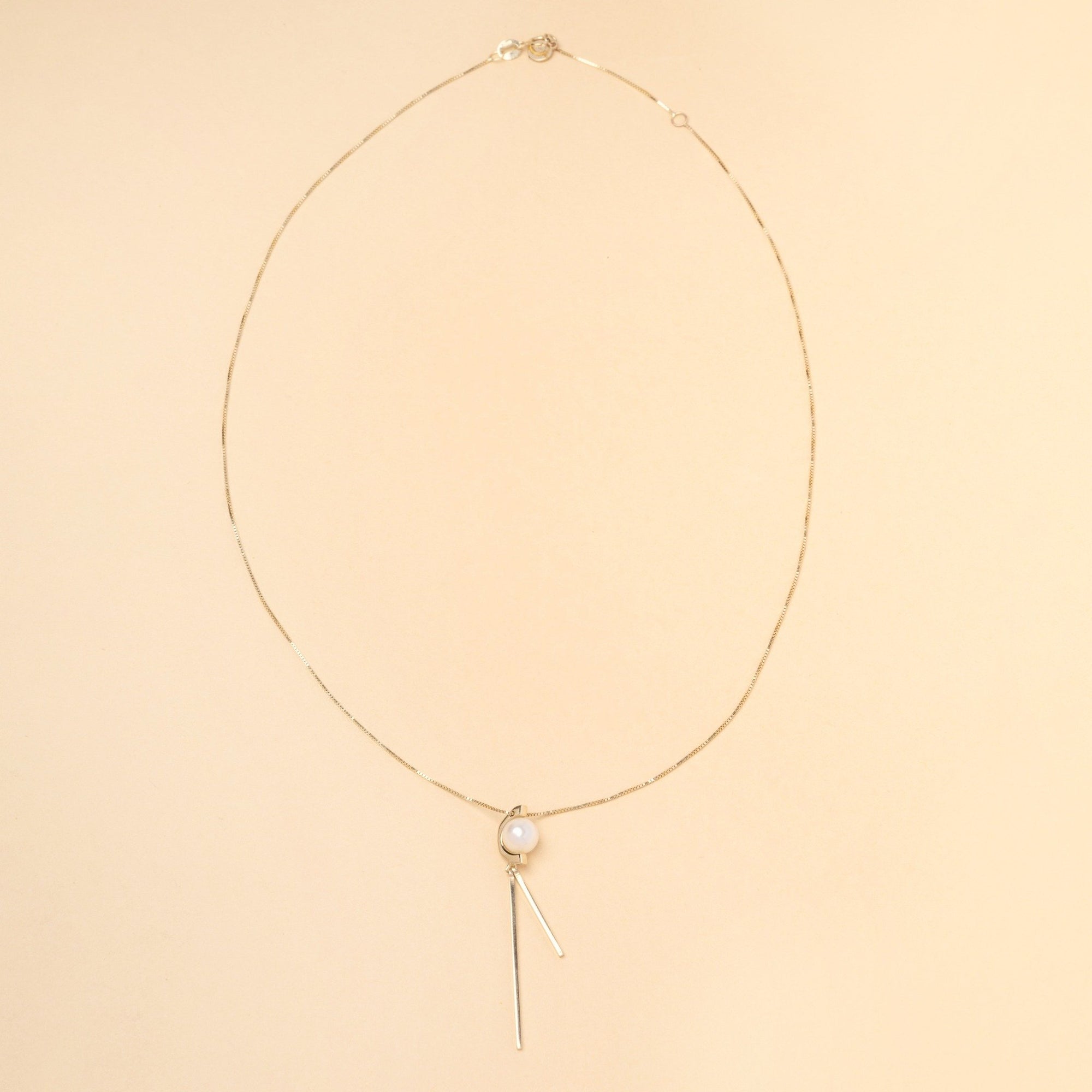 Tick & Tack Halsband i 14K Guld – flatlay med pärla, halvcirkel och två hängande rektangulära linjer.