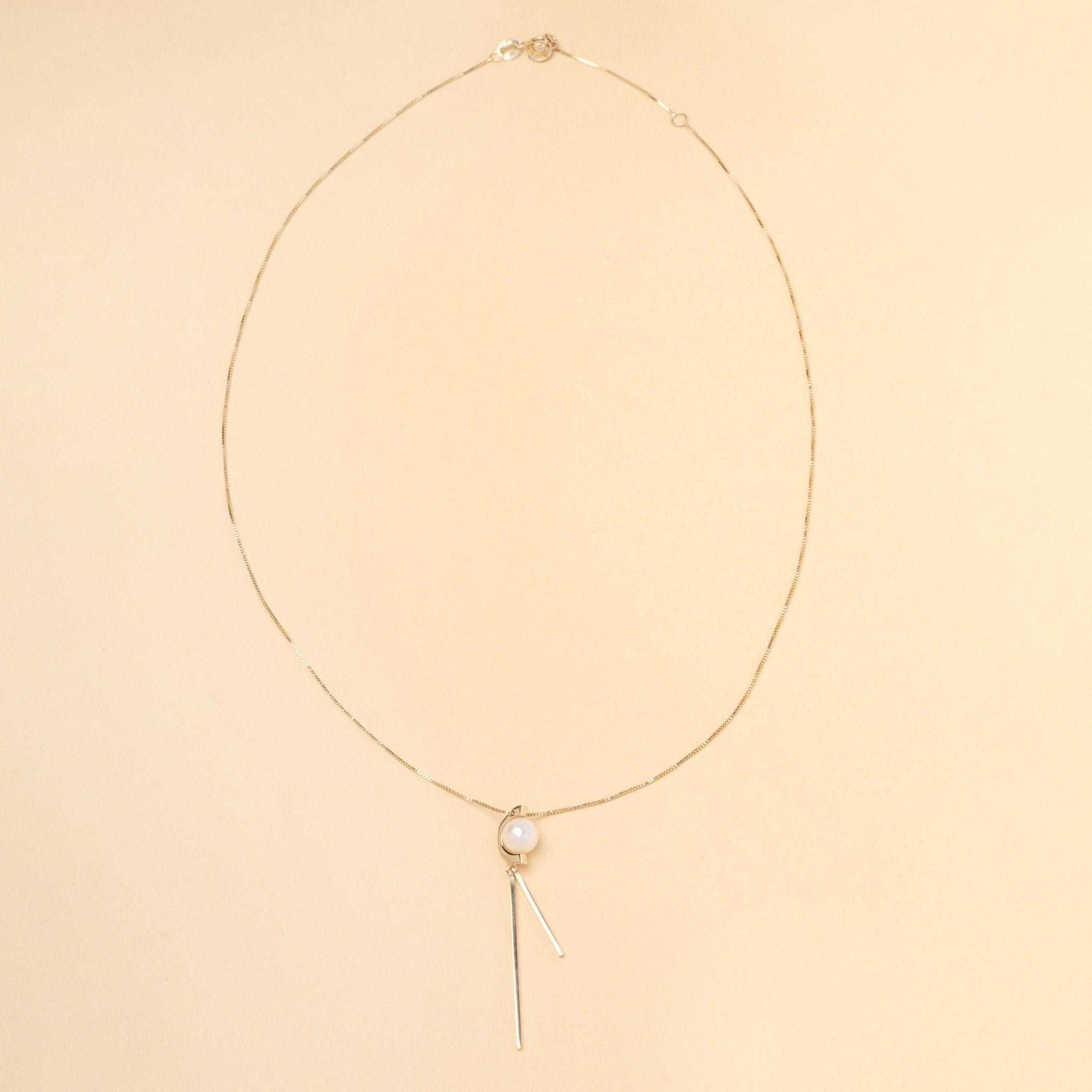 Tick & Tack Halsband i 14K Guld – flatlay med pärla, halvcirkel och två hängande rektangulära linjer.