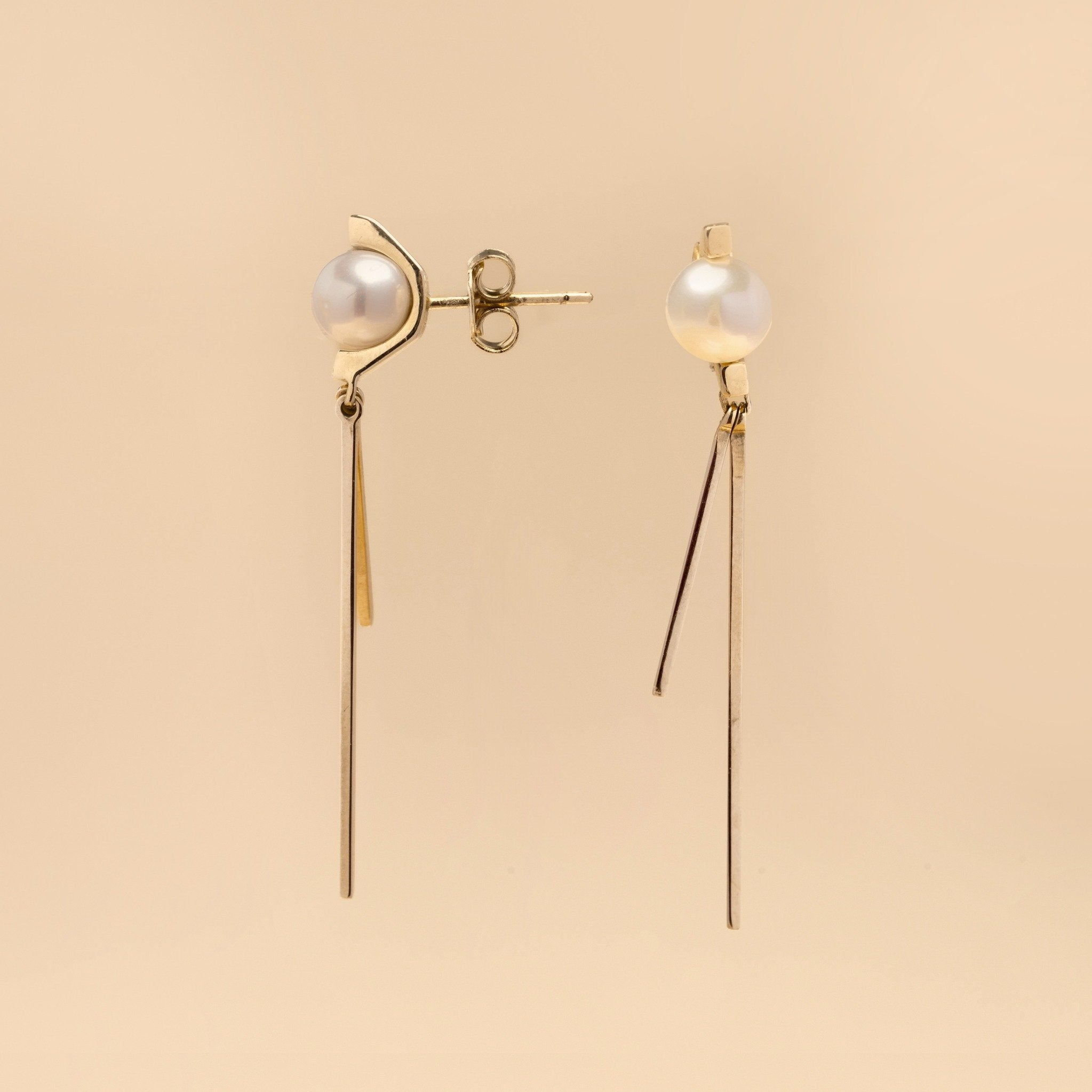Tick & Tack Örhängen i 14K Guld – pärla med halvcirkel och två hängande linjer, flatlay mot beige bakgrund.