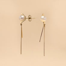 Tick & Tack Örhängen i 14K Guld – pärla med halvcirkel och två hängande linjer, flatlay mot beige bakgrund.